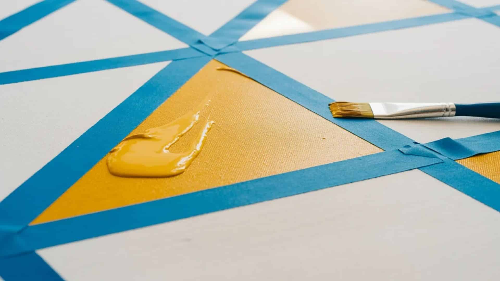 Geometric tape art in progress, with a yellow color block being painted inside a taped-off area